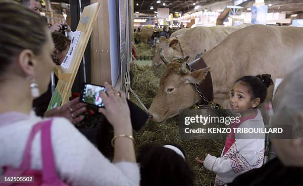 Woman takes a picture of a girl who gets ready to feed a cow as they visit the 50th International Agriculture Fair of Paris at the Porte de...