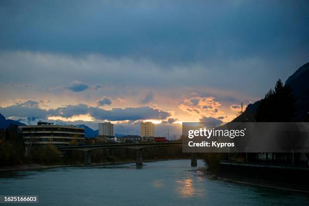 europe, austria, tyrol, kufstein, view of inn river and brandenberg austrian alps at dusk muslim woman walking, many refugees in this area - kufstein stock pictures, royalty-free photos & images