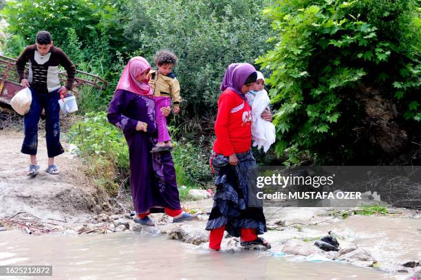 Syrian refugees cross a stream at a makeshift refugee camp in the northern Syrian city of Idlib near the Turkish village of Guvecci in Hatay on June...