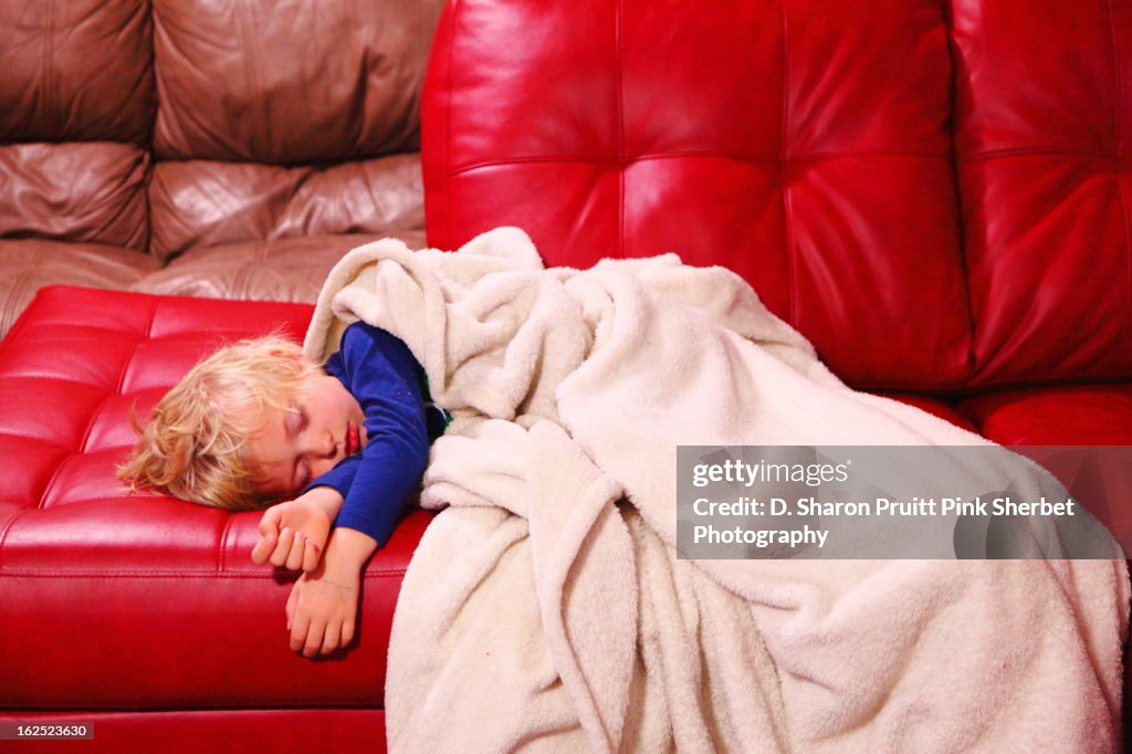 Four year old child sleeping on red sofa