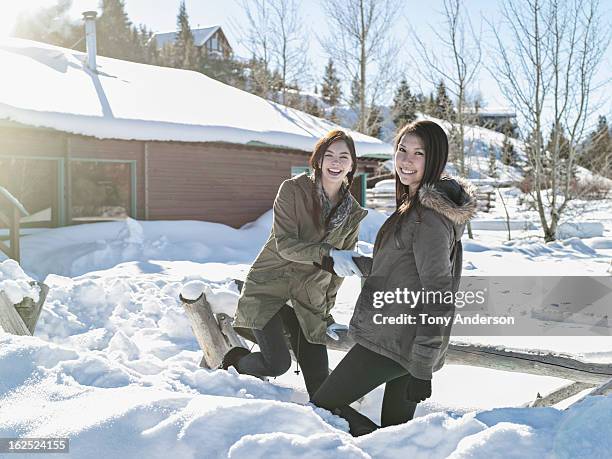 young women playing in snow near cabin - parka cappotto invernale foto e immagini stock