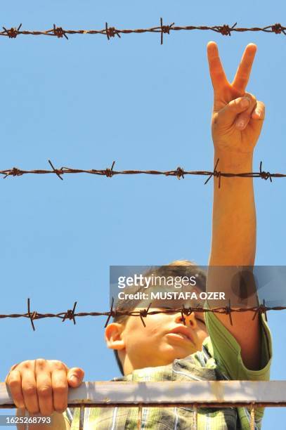 Syrian refugee boy flashes the victory sign behind a fence at the Turkish Red Crescent camp in the Altinozu district of Hatay, 30 kilometers from the...