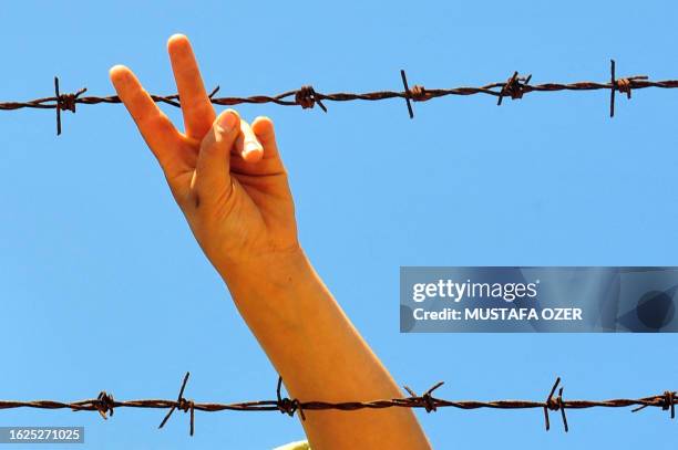 Syrian refugee boy flashes the victory sign as he stands behind a fence at the Turkish Red Crescent camp in the Altinozu district of Hatay, 30...