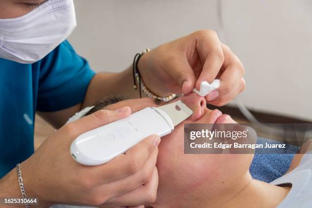 beautician does a skin cleansing on a woman's face with an ultrasonic spatula in her office - peeling off stock pictures, royalty-free photos & images