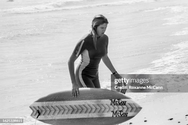 Australian surfer Pam Burridge emerges from the ocean carrying a McCoy surfboard and wearing a short-sleeved wetsuit after competing in the 1981...