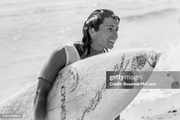 American surfer Debbie Beacham walks out of the water with a smile carrying an O'Neil surfboard and wearing a short-sleeved wetsuit at the 1981...