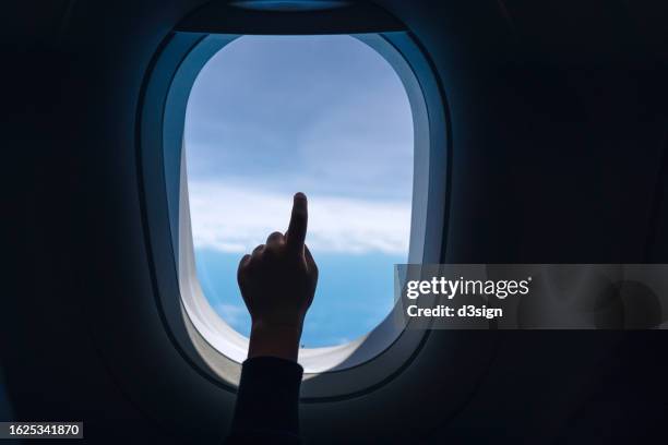 cropped shot of a little girl's hand pointing at airplane window against blue sky while travelling. travel and vacation concept - passenger cabin stock pictures, royalty-free photos & images