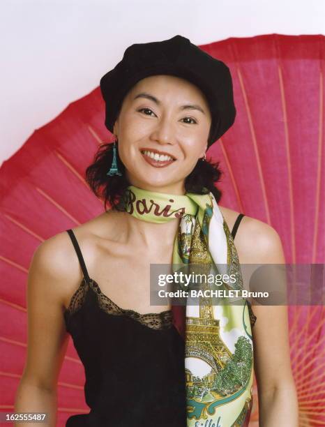 Maggie Cheung The Most Parisian Of Chinese Actresses. Photo studio de Maggie CHEUNG souriante, coiffée d'une casquette, un foulard marqué Paris...