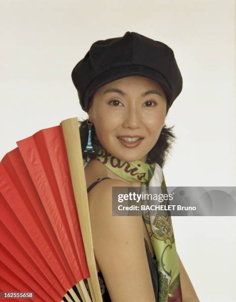 Maggie Cheung The Most Parisian Of Chinese Actresses. Photo studio de Maggie CHEUNG souriante, coiffée d'une casquette, un foulard marqué Paris...