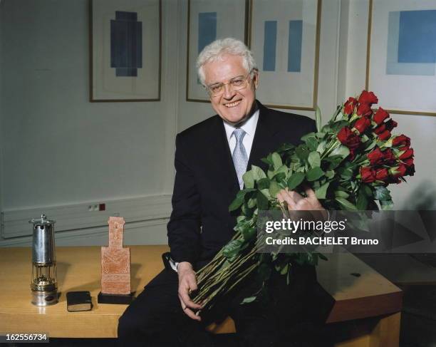 Lionel Jospin And His Fetish Objects. Lionel JOSPIN posant avec un bouquet de roses rouges dans les bras, assis sur un bureau sur lequel se trouvent...