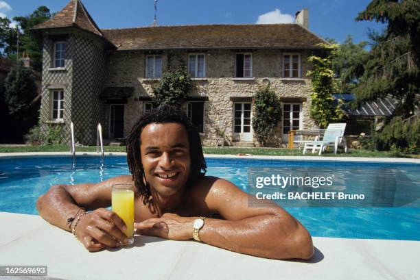 Yannick Noah At Home In Nainville Les Roches. A Nainville -les -Roches, devant sa maison, Yannick NOAH appuyé au rebord de sa piscine, un verre posé...