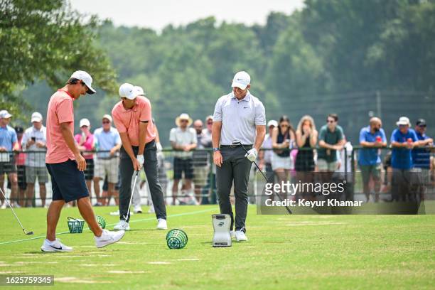 Rory McIlroy of Northern Ireland smiles as he looks at his Foresight GCQuad launch monitor with caddie Harry Diamond on the range next to Scottie...