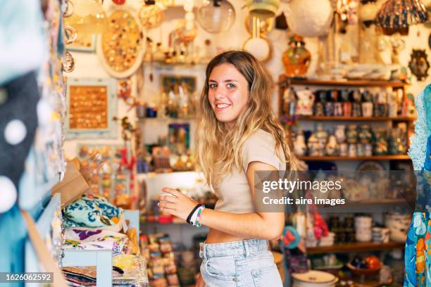 portrait of beautiful young woman standing smiling looking at the camera in casual clothes inside a souvenir store, side view - gift shop stock pictures, royalty-free photos & images