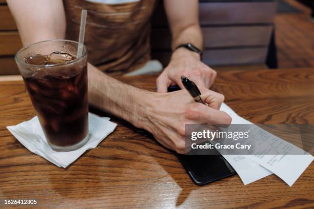 man signs credit card receipt at restaurant - gratuity - fotografias e filmes do acervo