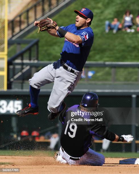 Charlie Blackmon of the Colorado Rockies slides under a leaping Ian Kinsler of the Texas Rangers at Salt River Field on February 25, 2013 in...