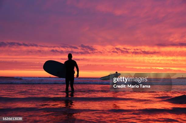 Surfers walk out of the Pacific Ocean at Ocean Beach shortly after sunset with Hurricane Hilary approaching on August 19, 2023 in San Diego,...