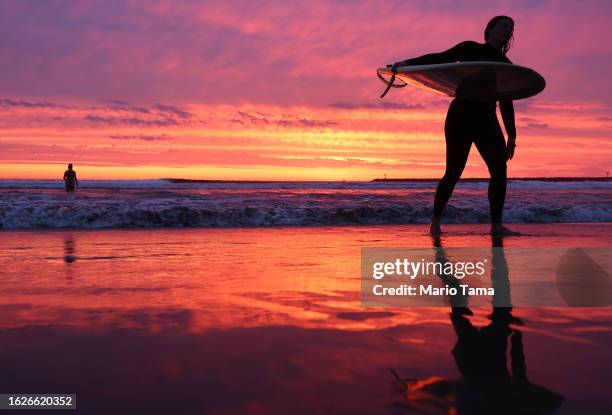 Surfer walks out of the Pacific Ocean at Ocean Beach shortly after sunset with Hurricane Hilary approaching on August 19, 2023 in San Diego,...
