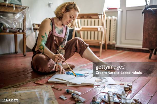 artistic journey: tattooed woman expressing herself with watercolors in her personal studio sitting on floor - body art painting fotografías e imágenes de stock