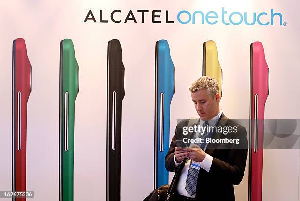 Visitor checks his smartphone beside an advertisement for the Alcatel-Lucent One Touch smartphone at the Mobile World Congress in Barcelona, Spain,...