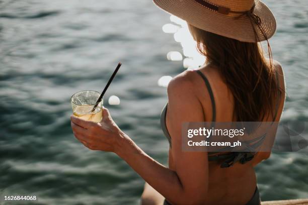 jeune femme coiffée d’un chapeau buvant des cocktails dans un bar de plage - straw stock photos et images de collection