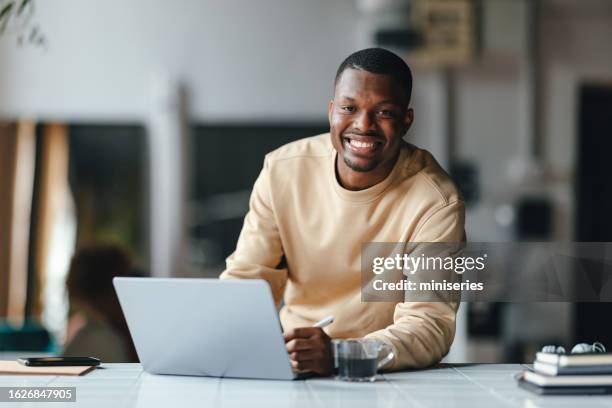 a happy businessman looking at camera while working on his computer - black man computer stock pictures, royalty-free photos & images