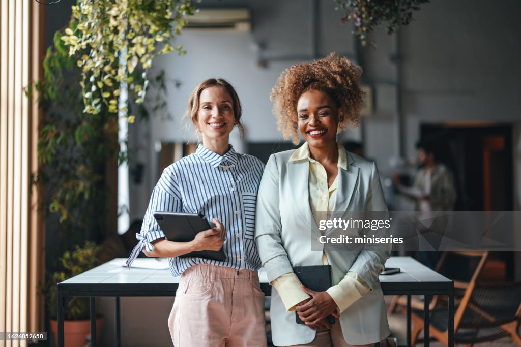 Two Happy Beautiful Blonde Businesswomen Looking At Camera While Standing In The Office