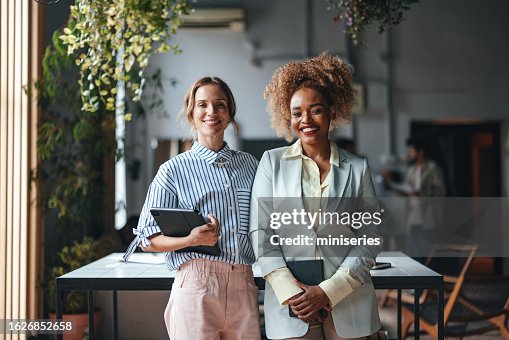 Two Happy Beautiful Blonde Businesswomen Looking At Camera While Standing In The Office Two Happy Beautiful Blonde Businesswomen Looking At Camera While Standing In The Office