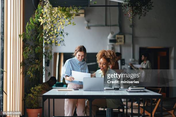 duas empresárias loiras bonitas felizes que trabalham no escritório usando seu computador - colega de trabalho papel humano - fotografias e filmes do acervo