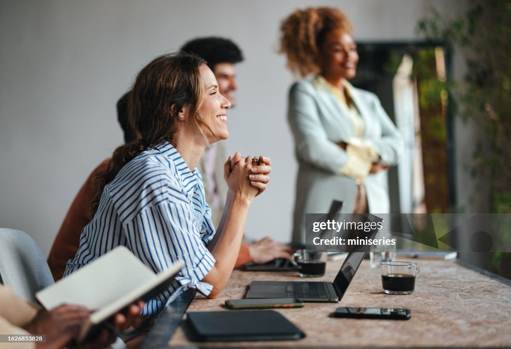 Eine glückliche schöne blonde Geschäftsfrau, die an ihrem Computer sitzt und ihrem Anführer zuhört