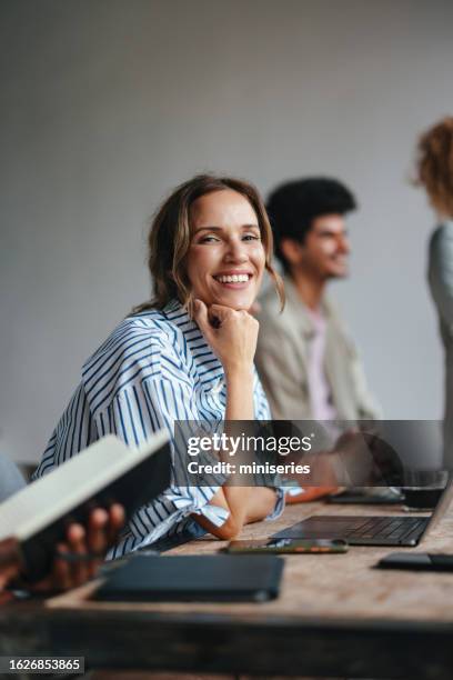 a happy beautiful blonde businesswoman looking at camera while sitting at her computer in the office - male colleague stock pictures, royalty-free photos & images