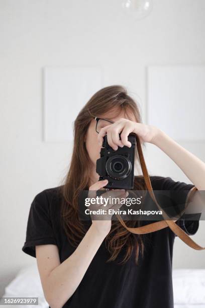 cute and young woman without a make-up with long brown hair in a black t-shirt looks in the mirror and takes a selfie on the camera - frauen mit fotoapparat stock-fotos und bilder