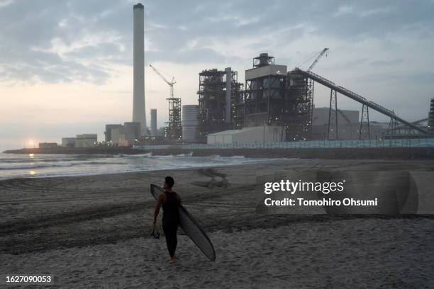 Surfer walks on the beach in front of the Hirono Thermal Power Station during the Iwasawa Surfing Games at Iwasawa beach on August 20, 2023 in...