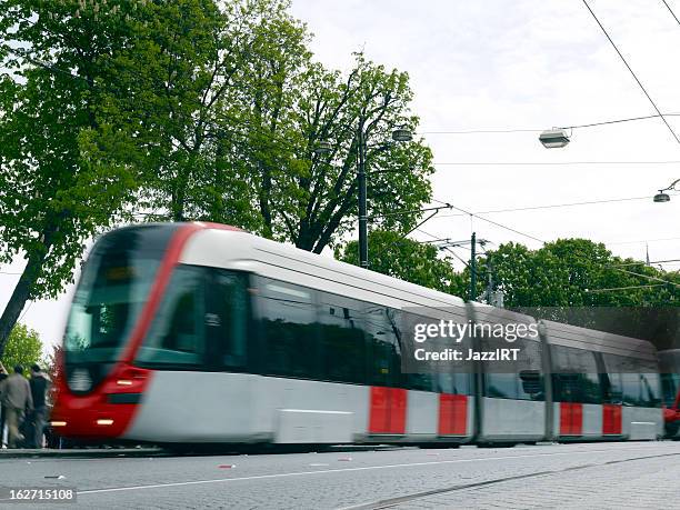 modern electric rail tram turning corner through trees. streetcar - trambaan stockfoto's en -beelden