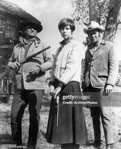 Armed John Wayne and Kim Darby standing next to Glen Campbell outside in a scene from the film 'True Grit', 1969.