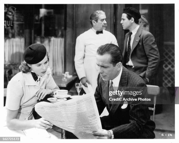 Ingrid Bergman and Humphrey Bogart looking at newspaper in restaurant in a scene from the film 'Casablanca', 1942.