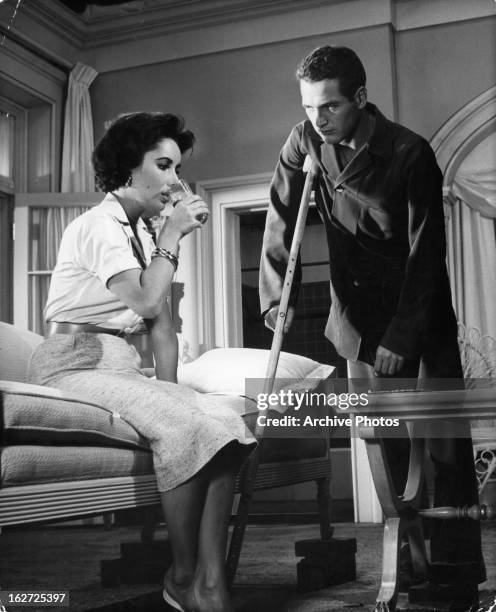 Elizabeth Taylor having drink as Paul Newman stands over her with one crutch in a scene from the film 'Cat On A Hot Tin Roof', 1958.