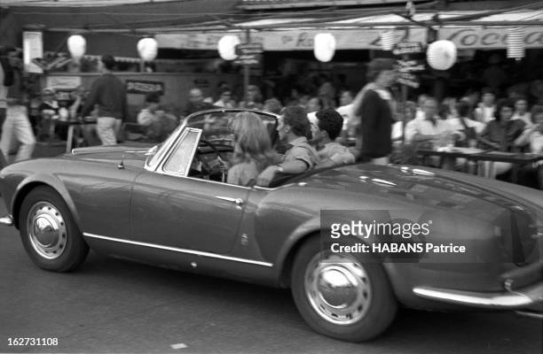 Holiday In Saint-Tropez. Les vacances à SAINT-TROPEZ, juillet 1961 : jeune femme au volant d'une Lancia Aurelia B24 décapotable devant les terrasses...