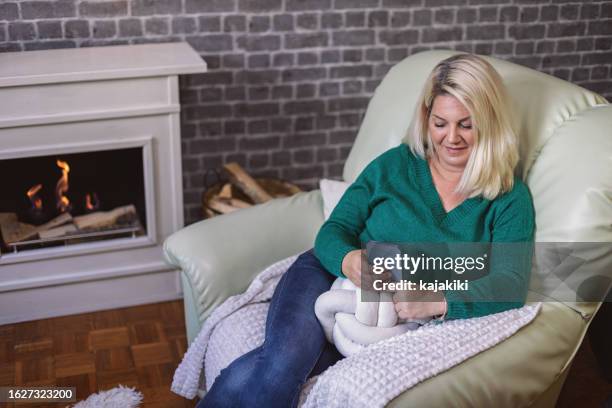 beautiful woman using her smartphone near the fireplace - mid adult women stock pictures, royalty-free photos & images