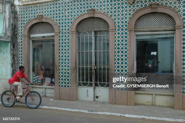 The Islands Of Sao Tome And Principe. Adolescent à vélo passant devant une boutique du centre-ville de SAO TOME, bâtiment de style portugais en pas...