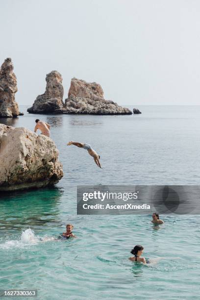 friends dive off cliffs into sea - sicilië stockfoto's en -beelden