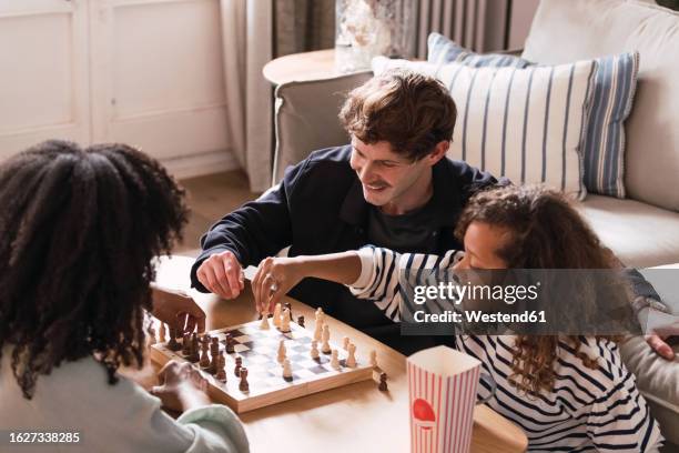 parents sitting in livingroom teaching daughter to play chess - family board game stock pictures, royalty-free photos & images
