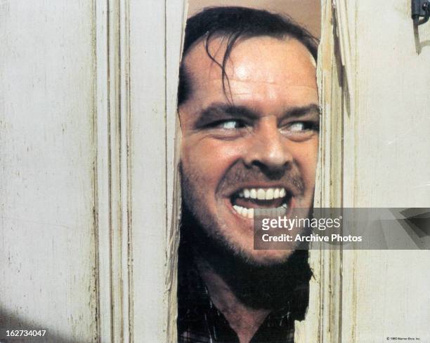 Jack Nicholson peering through axed in door in lobby card for the film 'The Shining', 1980.