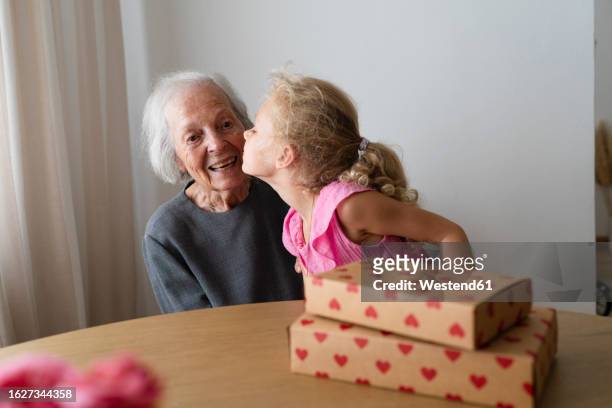 granddaughter kissing grandmother next to birthday present at home - arabian girl kissing stock-fotos und bilder