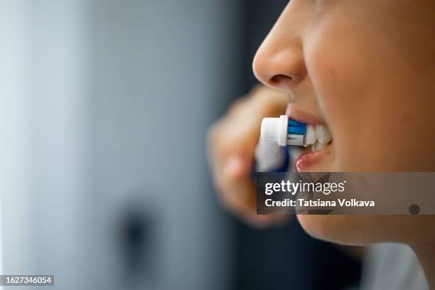 close up mouth of teenage boy holding electric toothbrush in hand, smiling and brushing teeth in bathroom. - lava foto e immagini stock