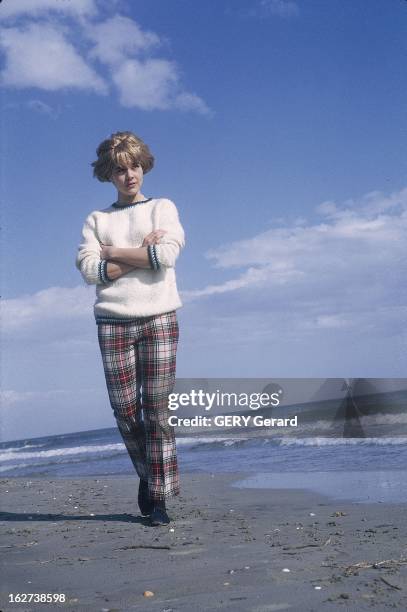 Close-Up Of Sylvie Vartan And Johnny Hallyday. Sylvie VARTAN bras croisés vêtue d'un pantalon à carreaux et d'un pull blanc se promenant sur la plage.