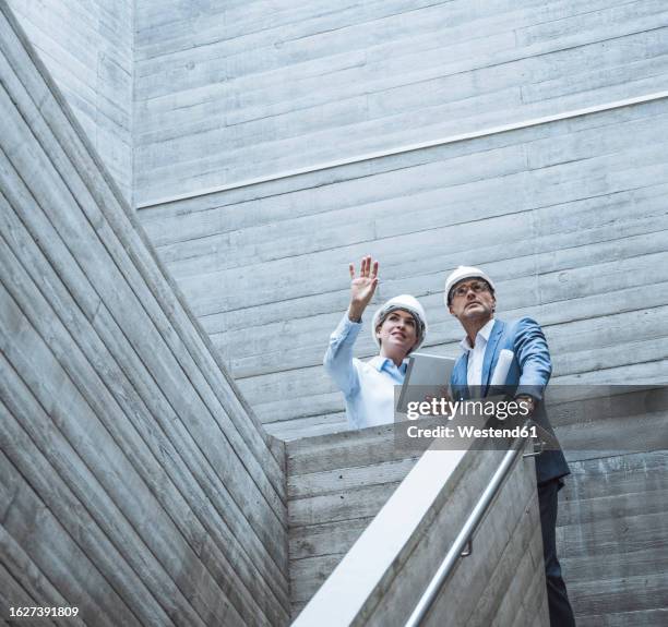 architect gesturing and having discussion with colleague on staircase - architekt mit plan frontal stock-fotos und bilder