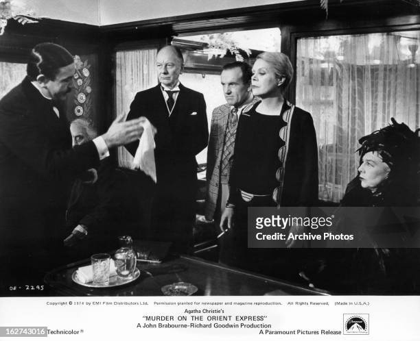 Albert Finney holds a napkin to Rachel Roberts in a scene from the film 'Murder On The Orient Express', 1974. John Gielgud stands behind.