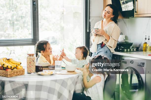 tired mother drinks coffee while her tree daughter has breakfast at home. - routine stockfoto's en -beelden