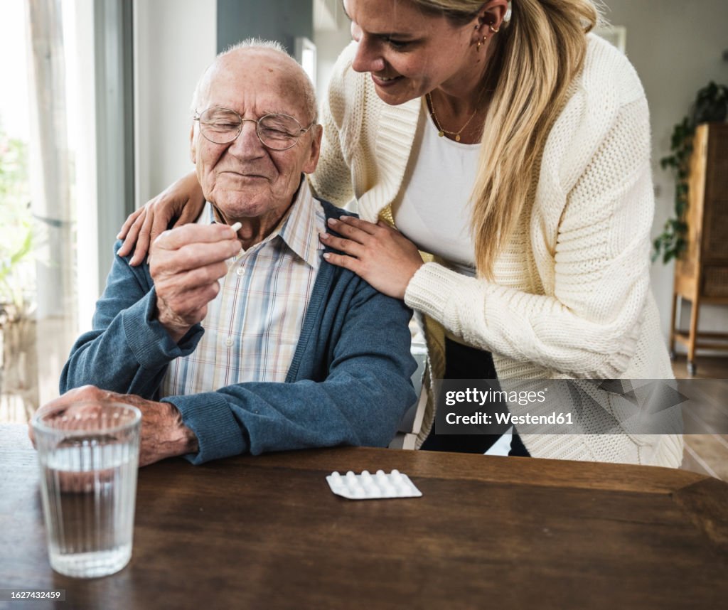 Smiling woman with senior man holding medicine at table