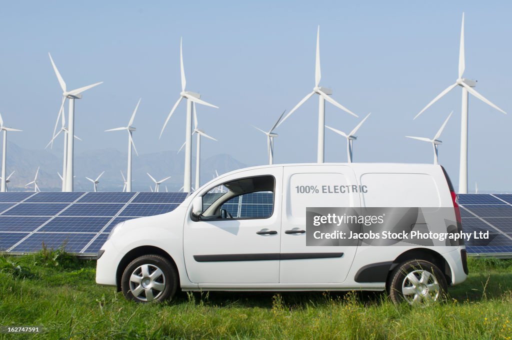 Electric van in front of solar panels and wind turbines